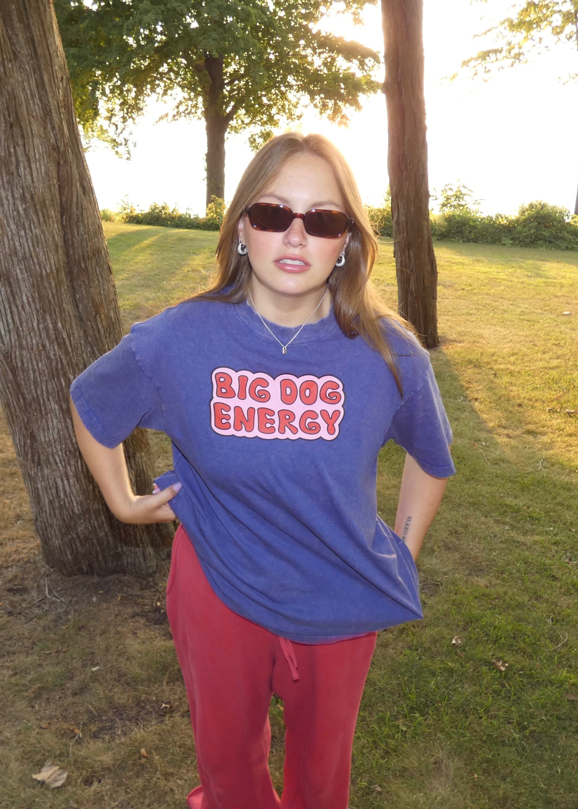 Woman wearing a blue t-shirt with 'BIG DOG ENERGY' text in a park setting