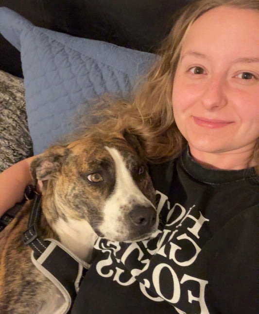 Person with a dog on a couch, wearing a black hoodie with  Hot Girl Rescue Dogs, white text 