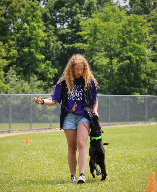 A woman wears a blue tee with text Hot Girl Rescue Dogs, and walks with a dog on a leash in an outdoor setting with trees in the background