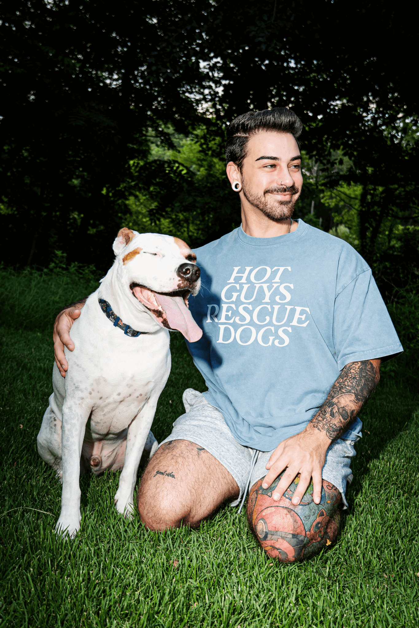 Man sitting on grass with a dog, wearing a 'Hot Guys Rescue Dogs' t-shirt.