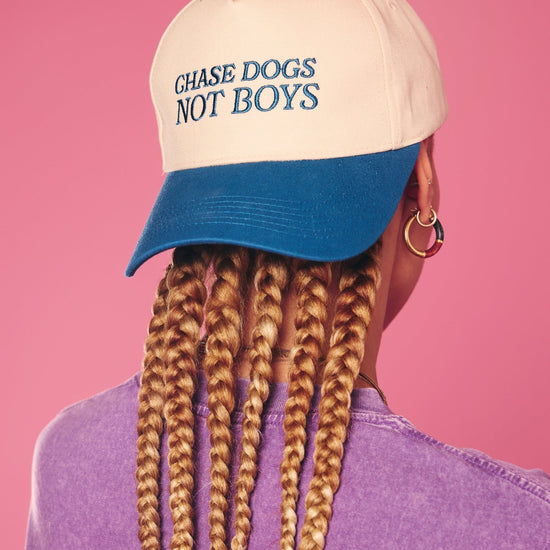 Person wearing a cap with 'Chase Dogs Not Boys' text on a pink background