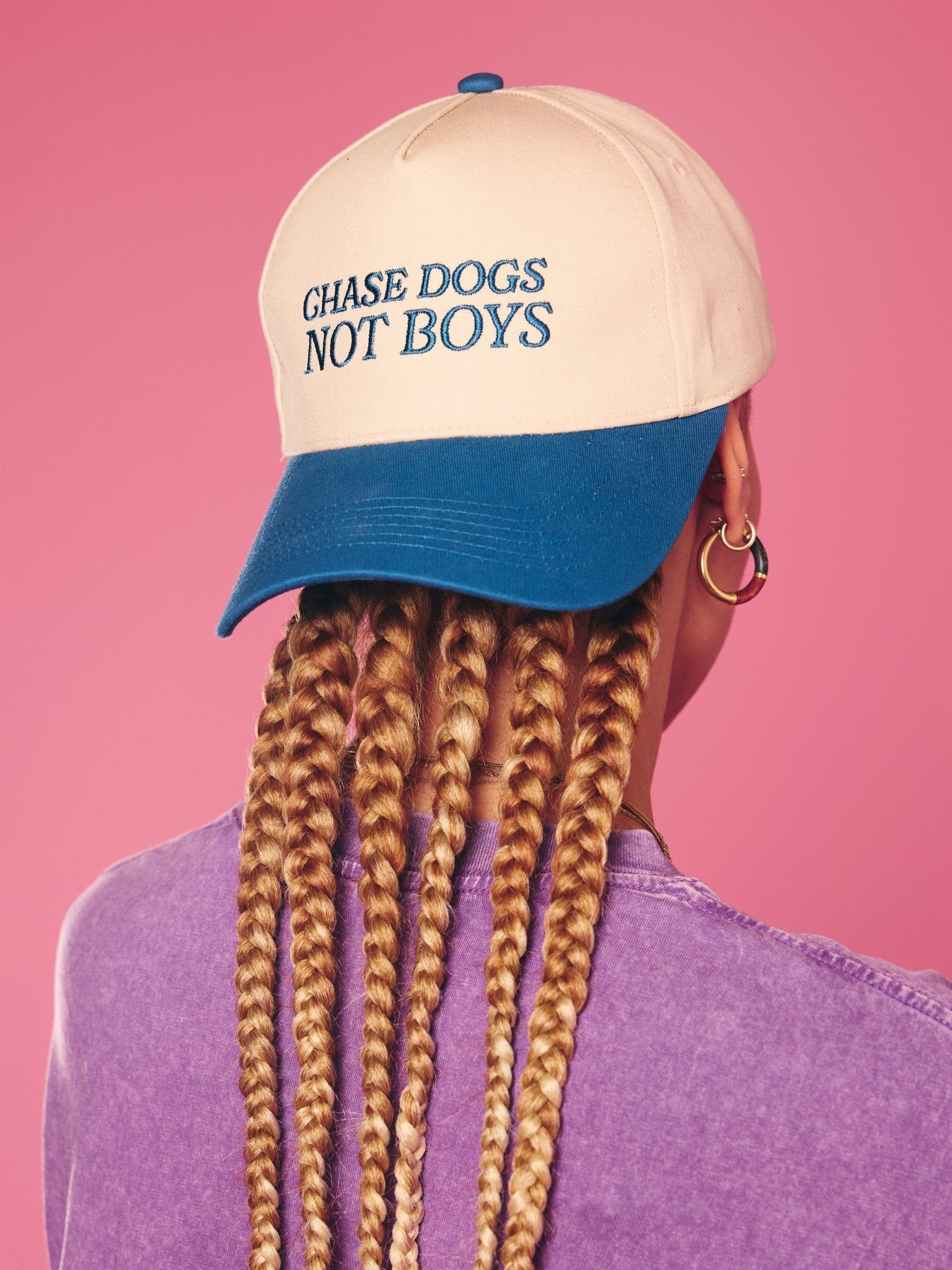 Person wearing a cap with 'Chase Dogs Not Boys' text on a pink background