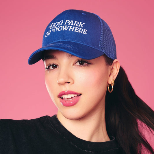 Person wearing a blue cap with 'Dog Park or Nowhere' text and a black shirt with 'Hot Girls' text against a pink background