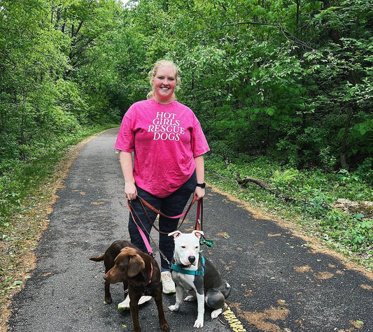 A Girl wearing a pink tee and walking with two dogs on a path surrounded by greenery 