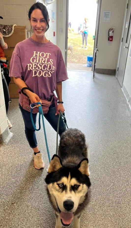A woman walking with a dog in an indoor setting, wearing a shirt with the text Hot Girl Rescue Dogs.