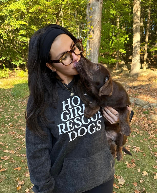 A girl wearing a hoodie with 'Hot Girls Rescue Dogs' text, holding a dog outdoors.