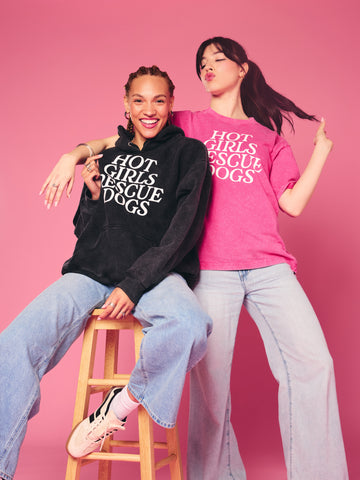 Two people wearing 'Hot Girls Rescue Dogs' shirts on a pink background