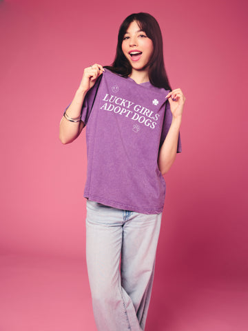 Woman holding a purple t-shirt with text against a pink background