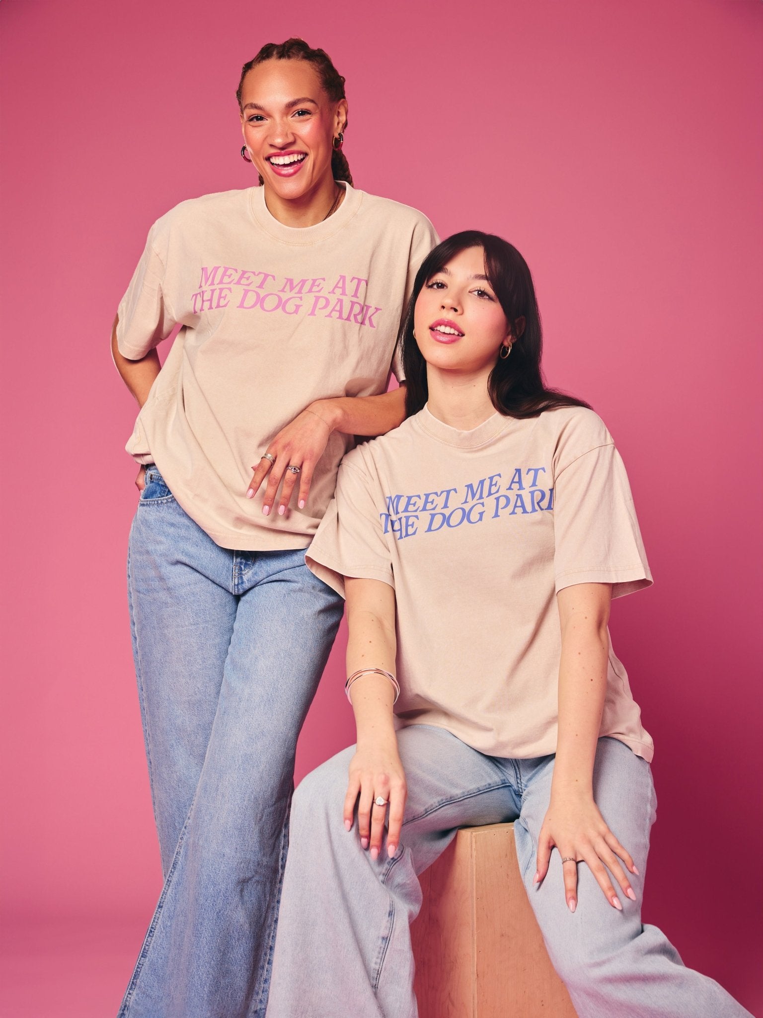 Two people wearing matching t-shirts with 'Meet Me at the Dog Park' text on a pink background