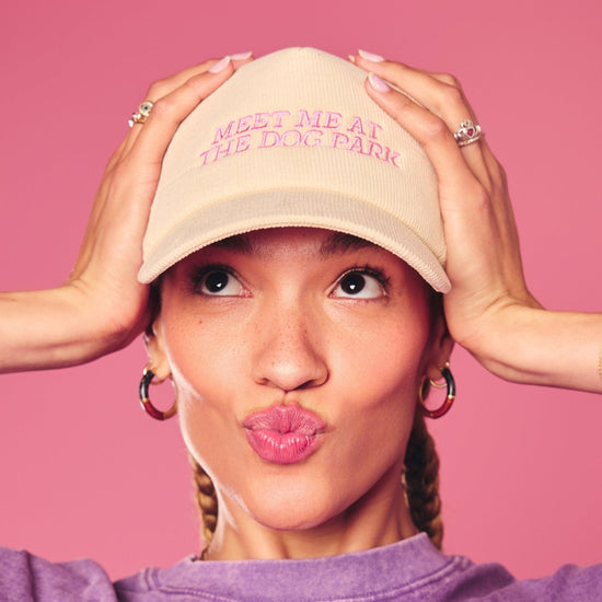 Person wearing a beige cap with pink Meet Me at the Dog Park Hat text on a pink background