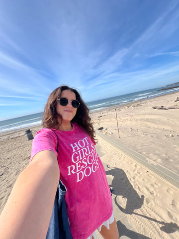 Person wearing a pink t-shirt with 'Hot Girls Rescue Dogs' on a beach
