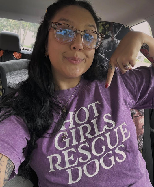 Person wearing a purple t-shirt with 'Hot Girls Rescue Dogs' text, sitting inside a vehicle.