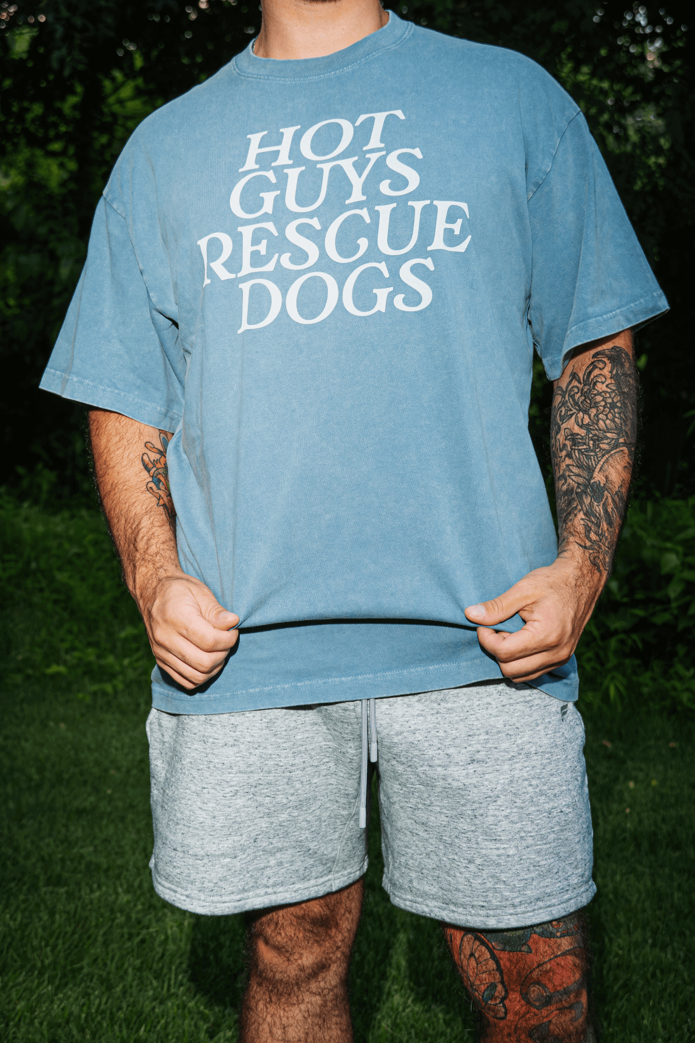 Person wearing a blue t-shirt with 'Hot Guys Rescue Dogs' text, standing outdoors.