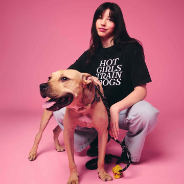 Person wearing a black t-shirt with text sitting on a pink background with a dog.